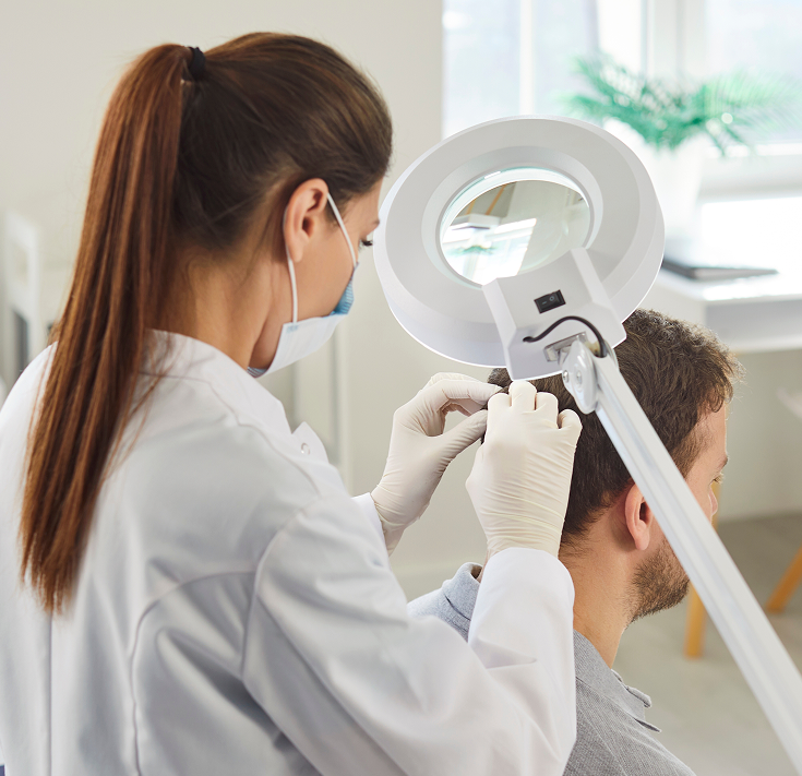 Dermatologist examining a patient's scalp with a specialized magnifying lamp in a bright clinical setting